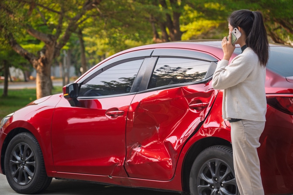 Woman standing next to her crashed car with her phone to her ear, asking about whether she needs a lawyer for a car accident if she wasn’t at fault.