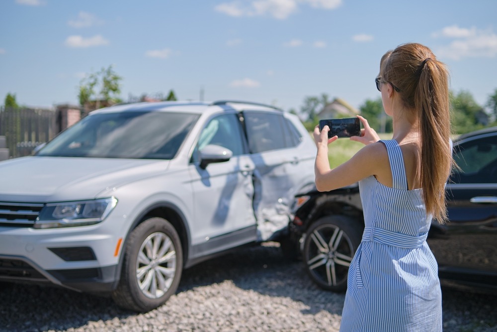 A woman taking a photo of her car accident with her phone, wondering how to get a car crash report in Bellevue, WA.